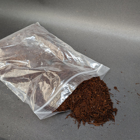 Clear resealable bag of dark brown tree fern fiber with loose material spilled nearby.